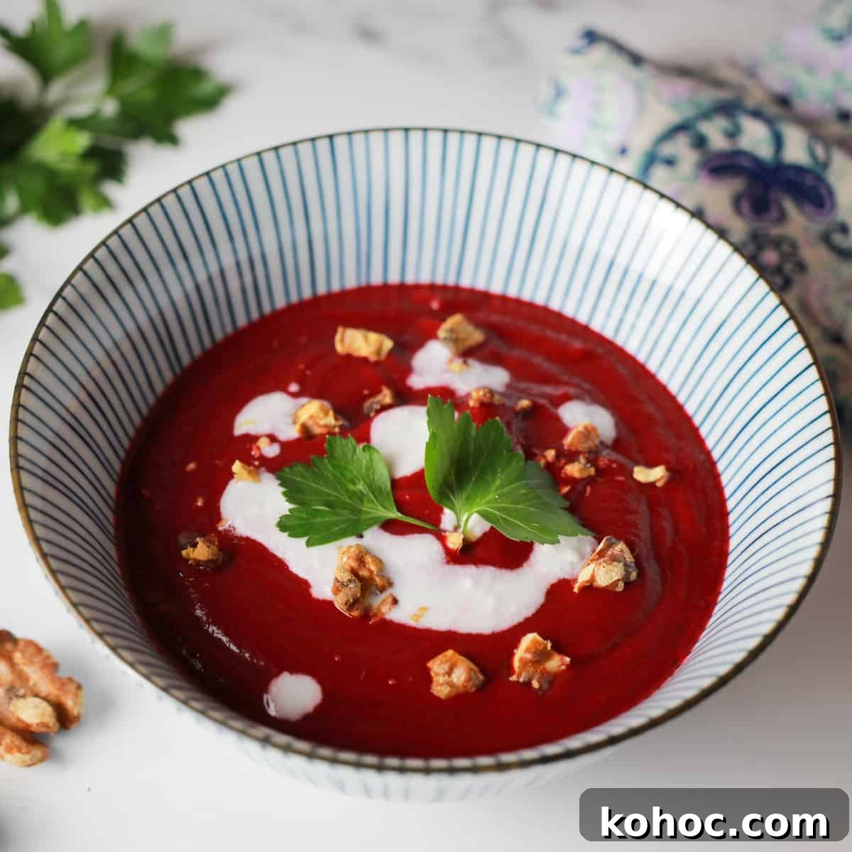 Roasted Beet and Walnut Soup Recipe — Comforting Autumn Starter 6 photo of a blue and white striped bowl with deep pink beetroot and walnut soup and dotted with coconut cream, walnut pieces and a sprig of parsley.