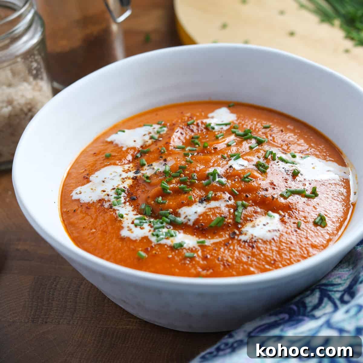 Photo of a bowl of tomato, lentil and squash soup with vegan cream swirled on top and chopped chives.