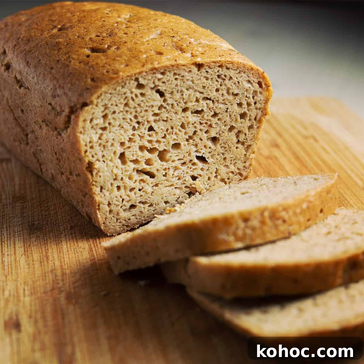 a loaf of vegan gluten free bread with three slices cut and fallen flat on the chopping board in front of the loaf showing the open crumb inside.