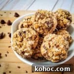 Side shot of multiple energy balls in a white bowl on a cutting board sprinkled with flax seeds and chocolate chips.