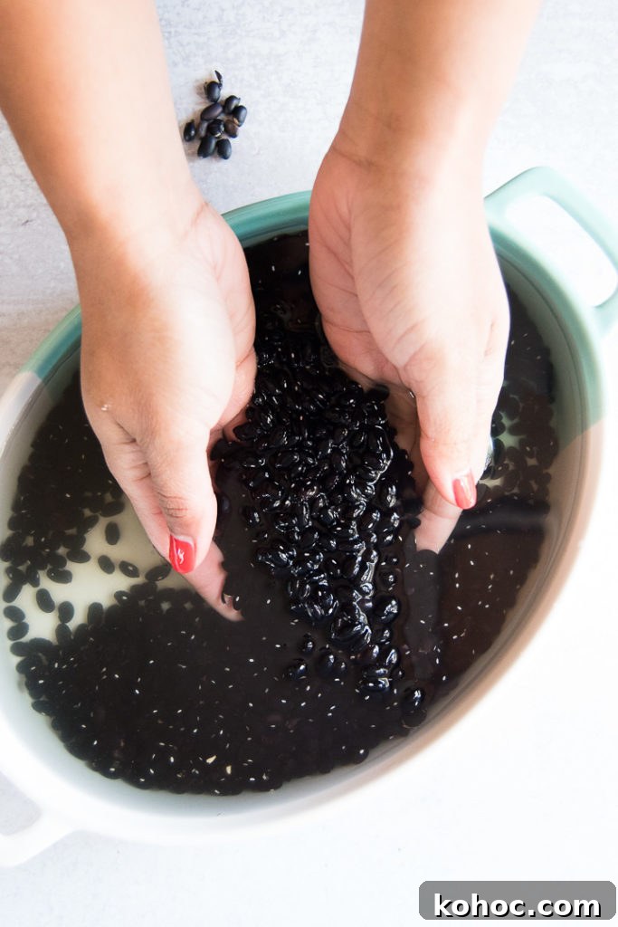 A woman holds and lifts a bunch of black beans in water from a blue and white dish. There are a few broken beans on the table off the background. 