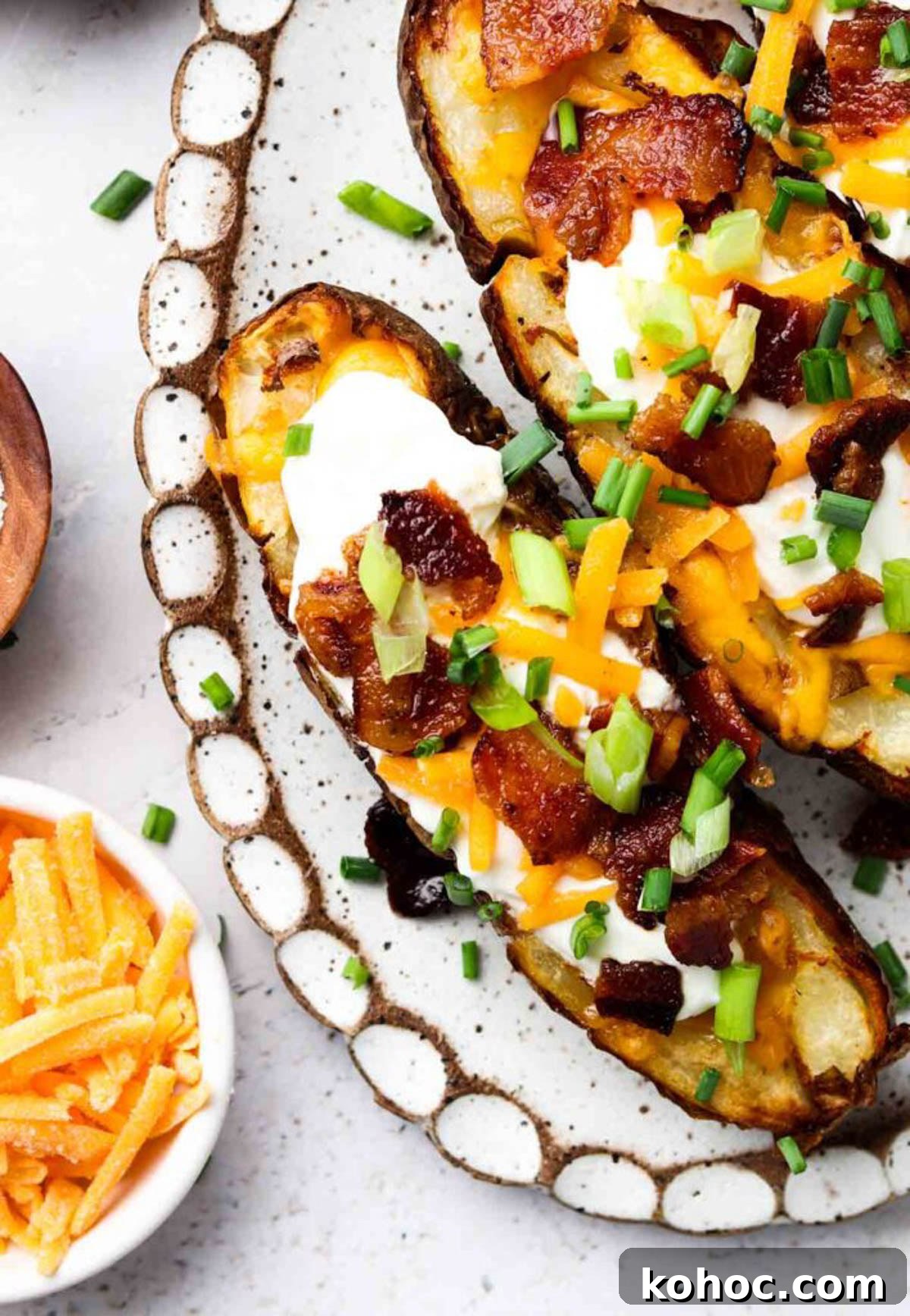 Crispy Air Fryer Potato Skins with Cheddar & Bacon 2 Air fryer potato skins on a plate garnished with fresh green onions and chives.