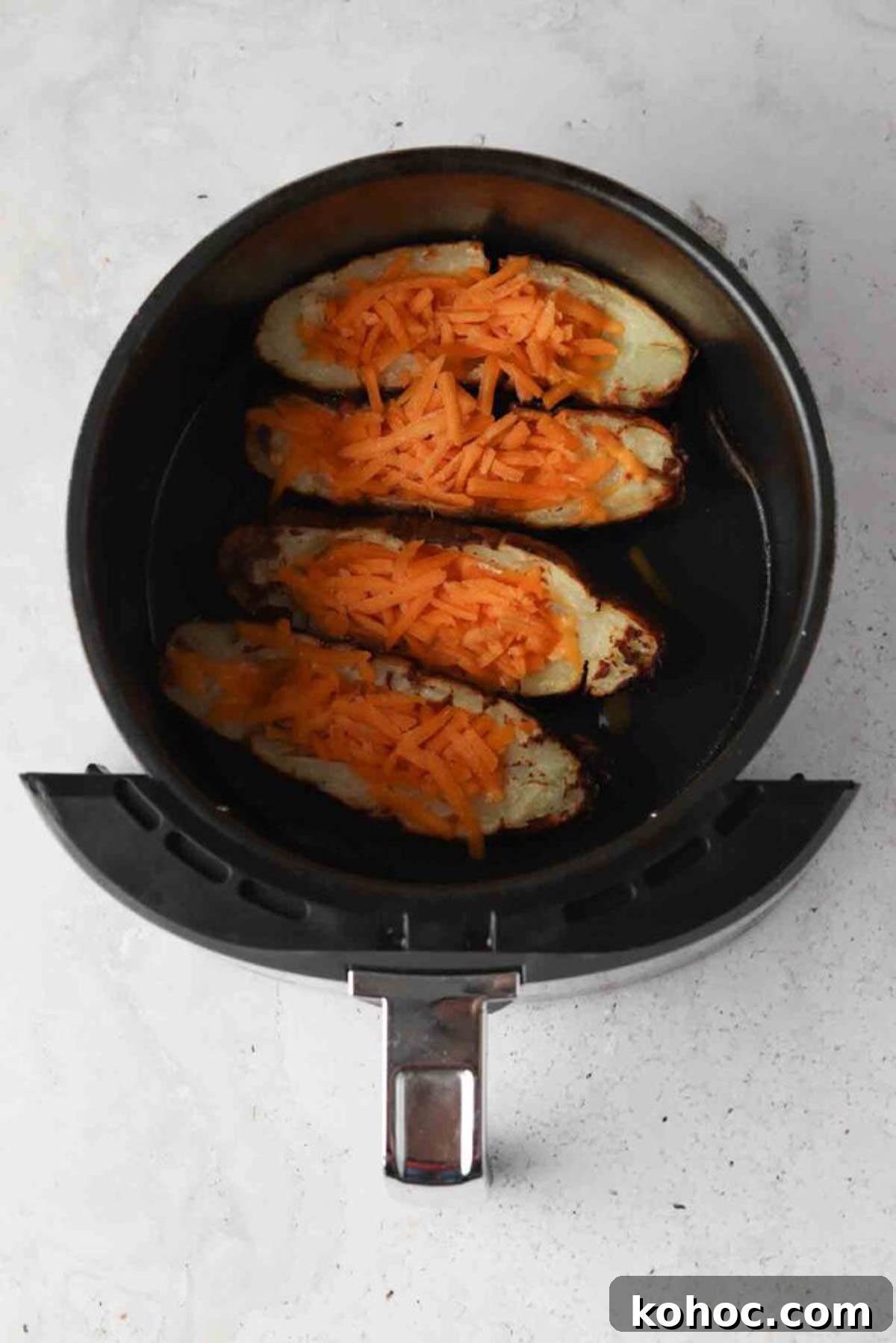 Crispy Air Fryer Potato Skins with Cheddar & Bacon 6 Halved potato skins in an air fryer basket with shredded cheese on top.