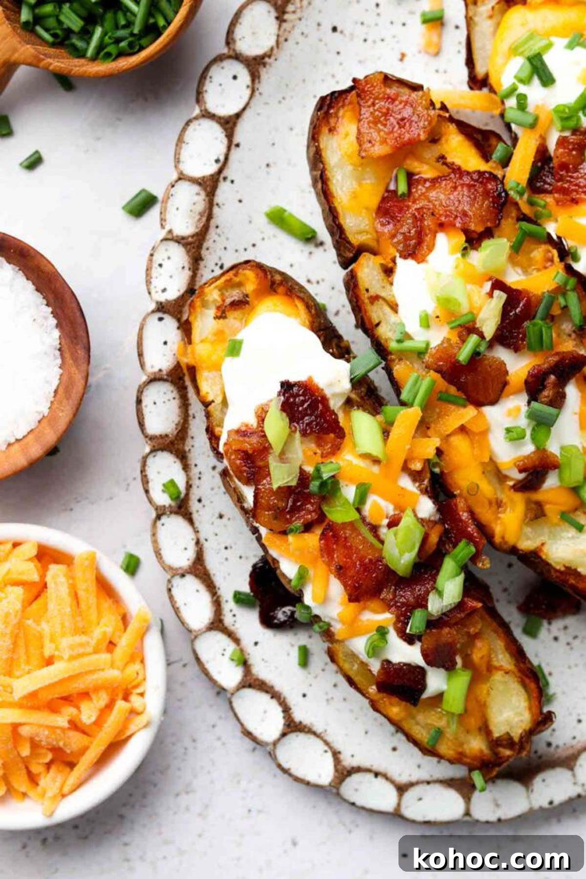 Crispy Air Fryer Potato Skins with Cheddar & Bacon 7 Air fryer potato skins on a plate garnished with bacon, sour cream, and fresh herbs.