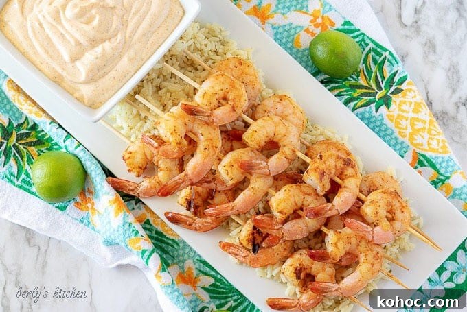 An aerial photo of the finished grilled shrimp on skewers, served over rice, on a rectangular white plate.