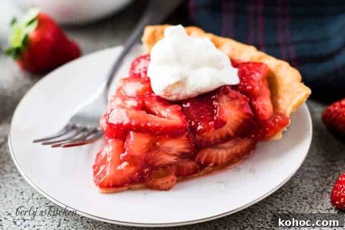 The strawberry pie topped with whipped cream on a plate.