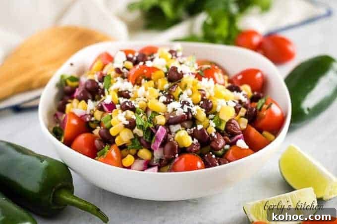 A bowl filled with corn and black bean salsa garnished with limes.