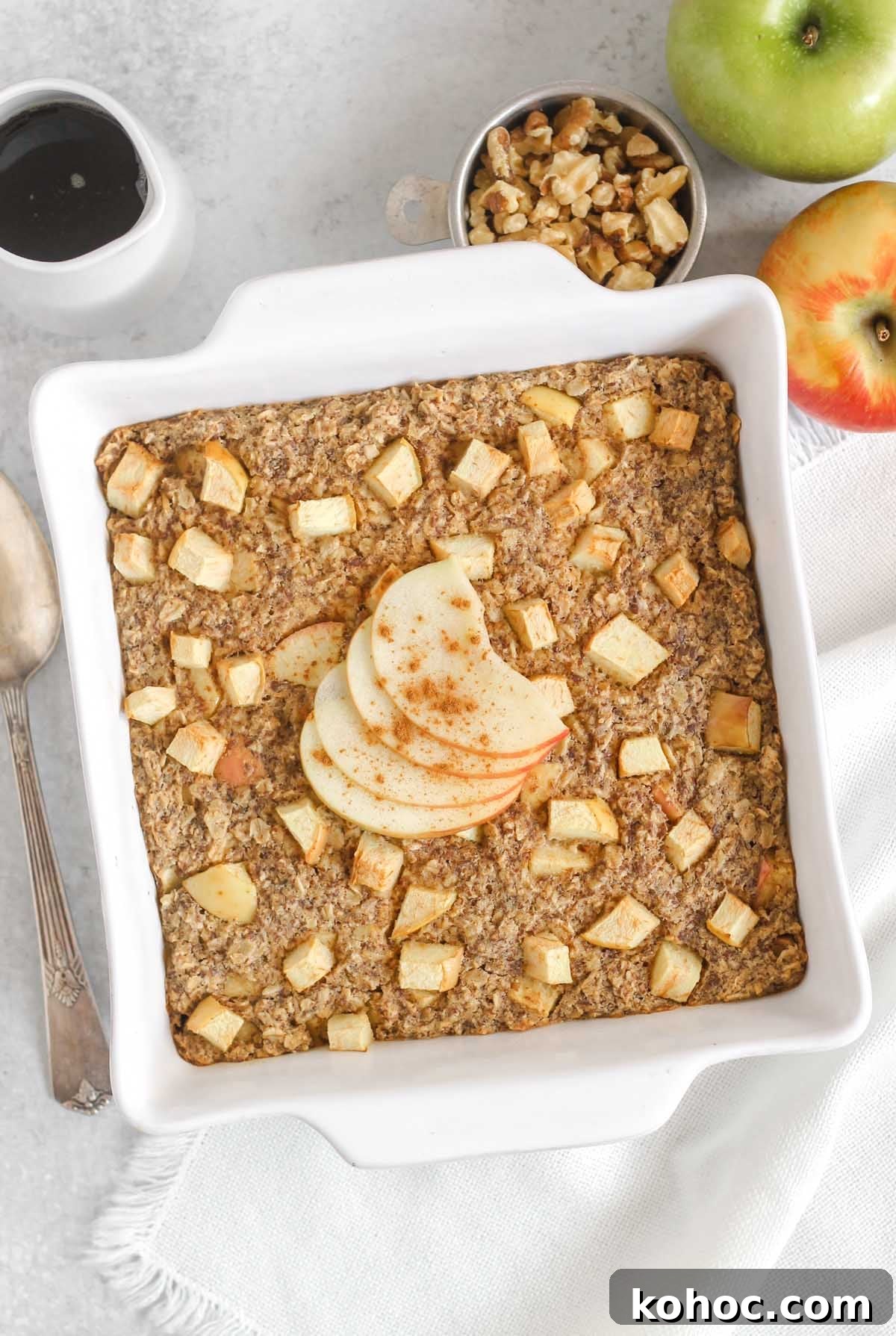 Apple Cinnamon Baked Oatmeal Recipe for Cozy Breakfasts 2 Apple cinnamon baked oatmeal topped with apple sliced and cinnamon in a white square baking dish with apples and syrup off to the side.