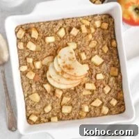 Apple Cinnamon Baked Oatmeal Recipe for Cozy Breakfasts 14 Baked apple oatmeal topped with apple slices in a square white baking dish with apples and syrup on the side.