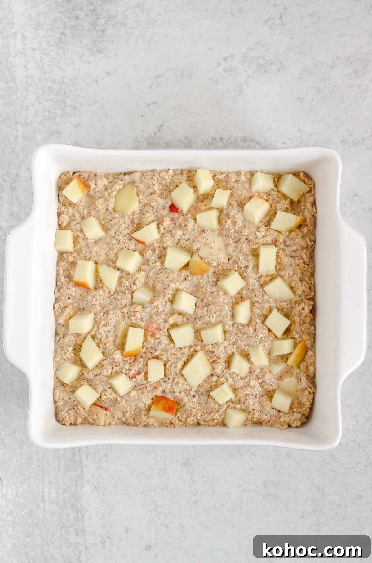 Apple Cinnamon Baked Oatmeal Recipe for Cozy Breakfasts 6 Oatmeal batter in a square white baking dish sprinkled with apple pieces.