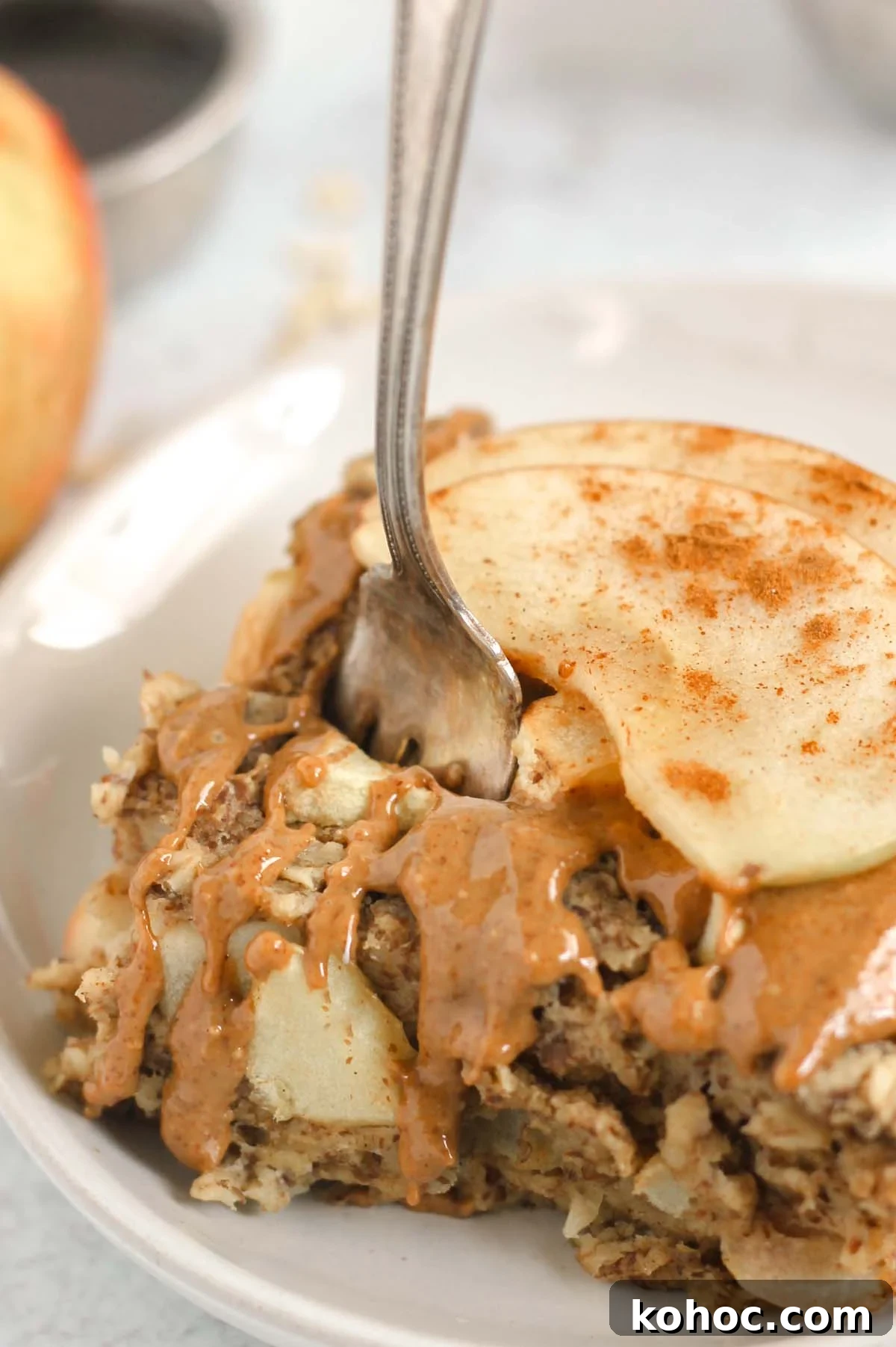 Apple Cinnamon Baked Oatmeal Recipe for Cozy Breakfasts 8 Fork taking a bite out of a square piece of apple baked oatmeal topped with sliced apples and almond butter.