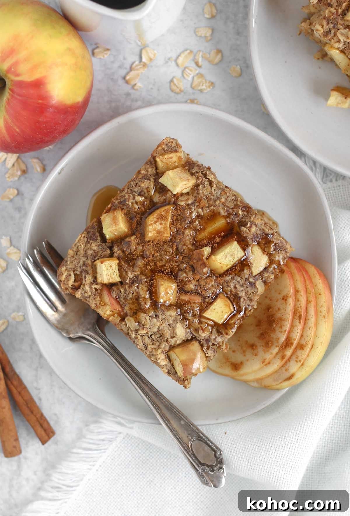 Apple Cinnamon Baked Oatmeal Recipe for Cozy Breakfasts 9 Square piece of apple cinnamon baked oatmeal topped maple syrup on a round plate with a vintage fork.