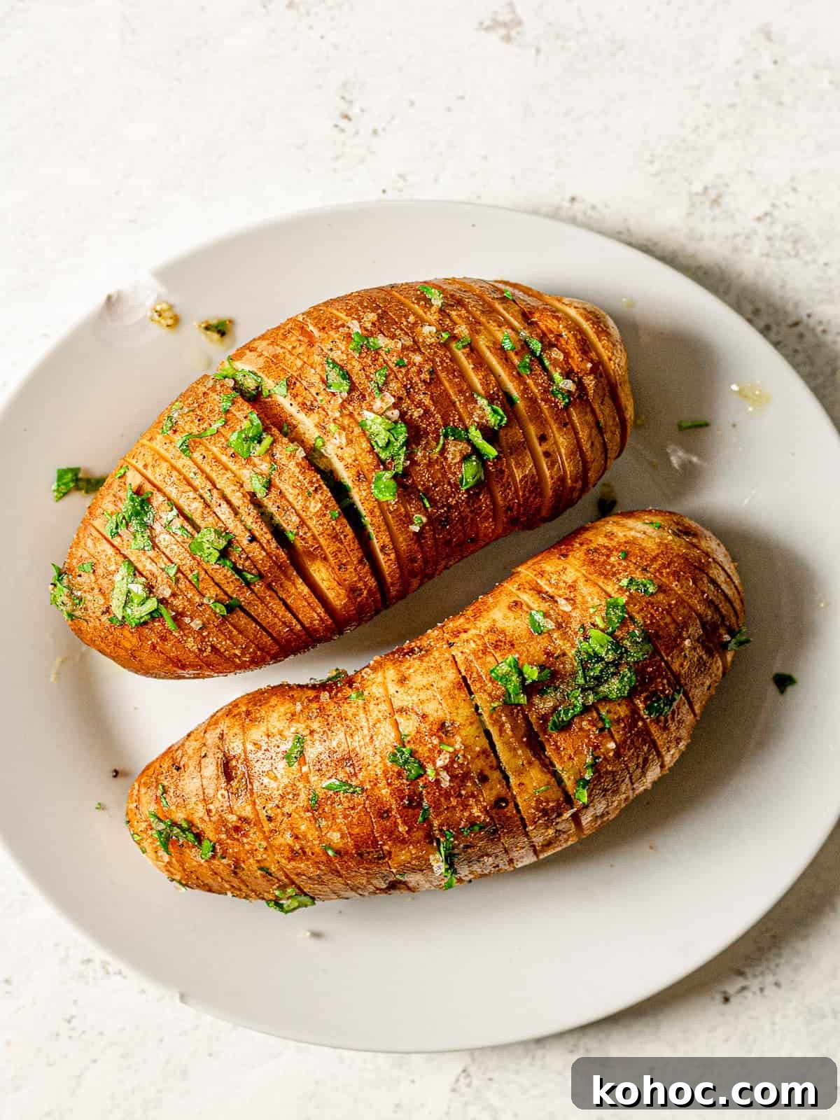 Crispy Air Fryer Hasselback Potatoes with Garlic and Herbs 5 Uncooked hasselback potatoes on a white plate.