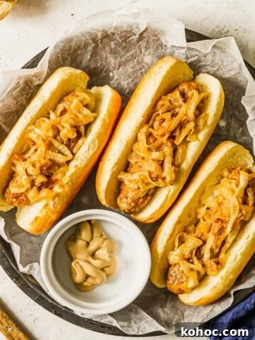 Three sausages topped with caramelized onions with a bowl of Dijon mustard.