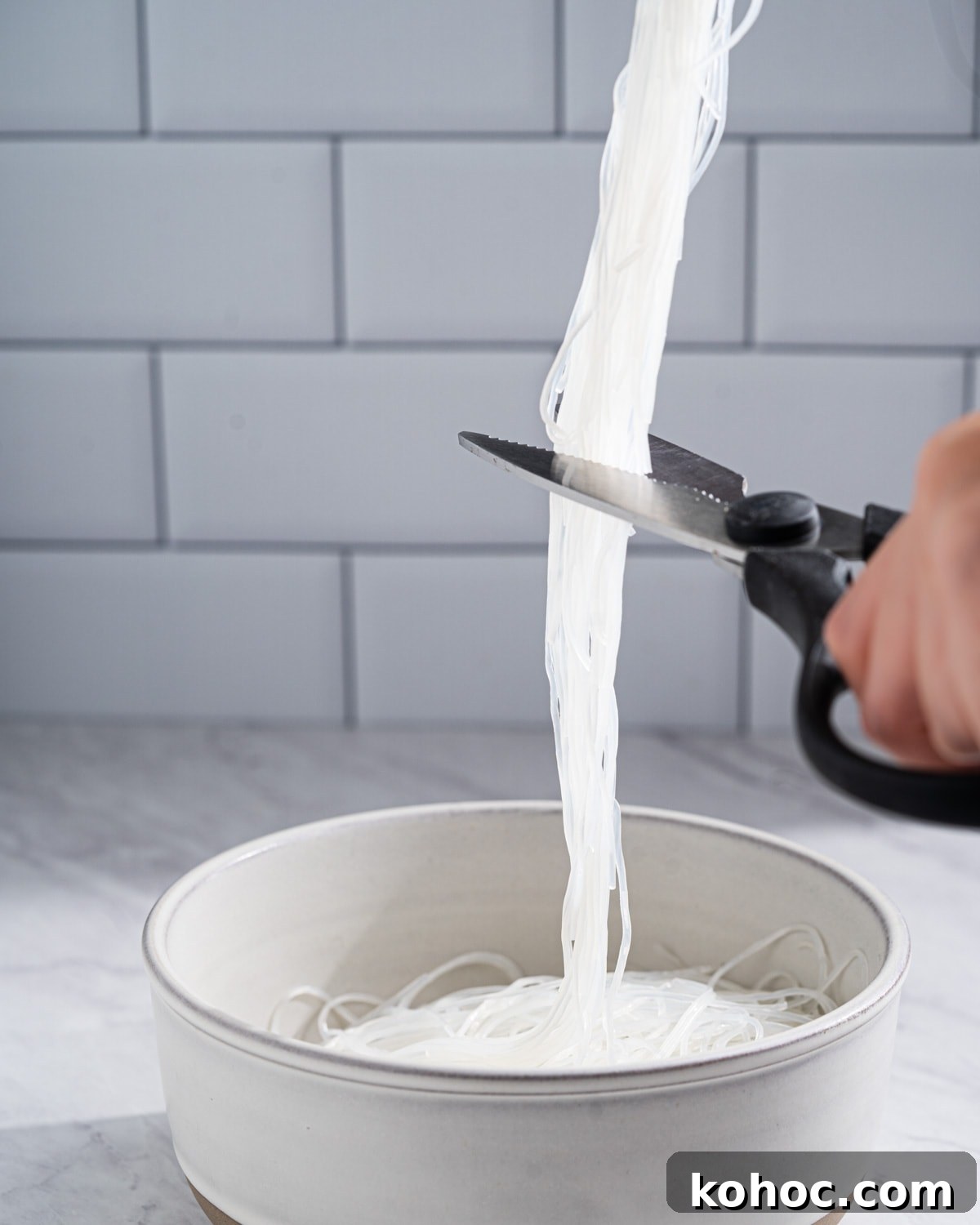 Perfect Rice Noodles: How to Cook Them Without Overcooking 9 holding long strands of cooked vermicelli with scissors and cutting in half.