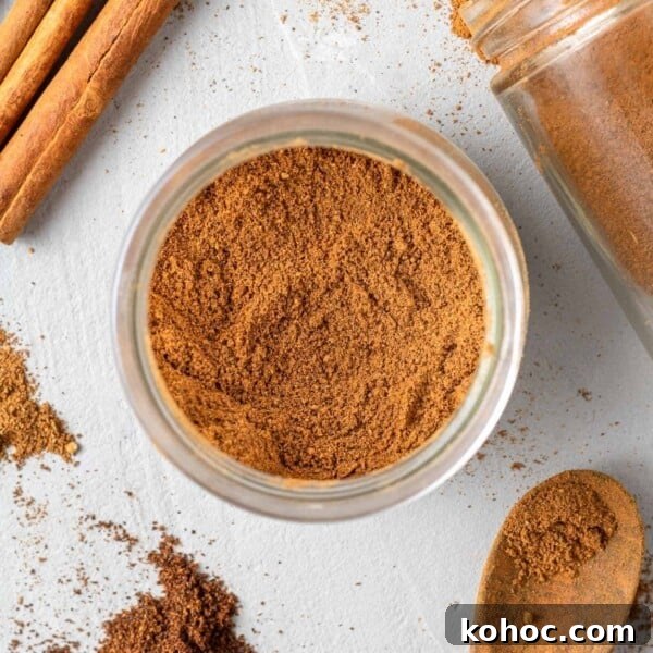 Overhead view of pumpkin pie spice in a small jar, cinnamon sticks nearby.