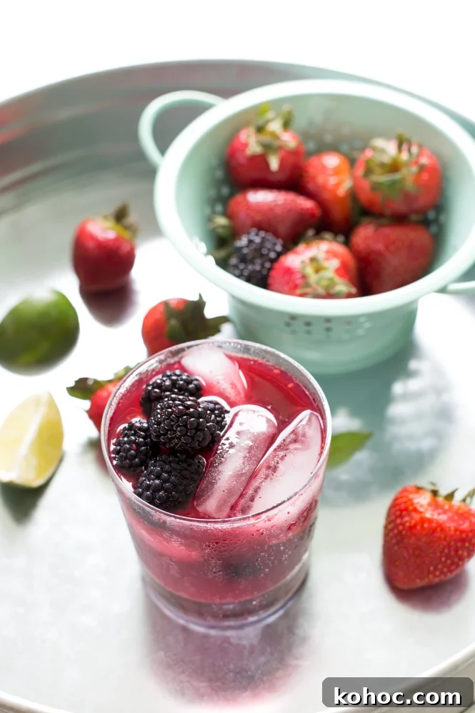 Mixed Berry Mojito Recipe: Refreshing Berry Mint Cocktail 5 close up of Mixed Berry Mojito garnished with mint, berries scattered on table, colander in background