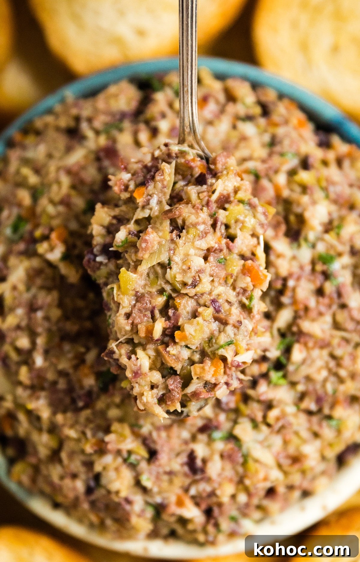 Creamy Artichoke and Olive Dip Recipe 8 A spoon holding up a spoonful of olive tapenade from the bowl.