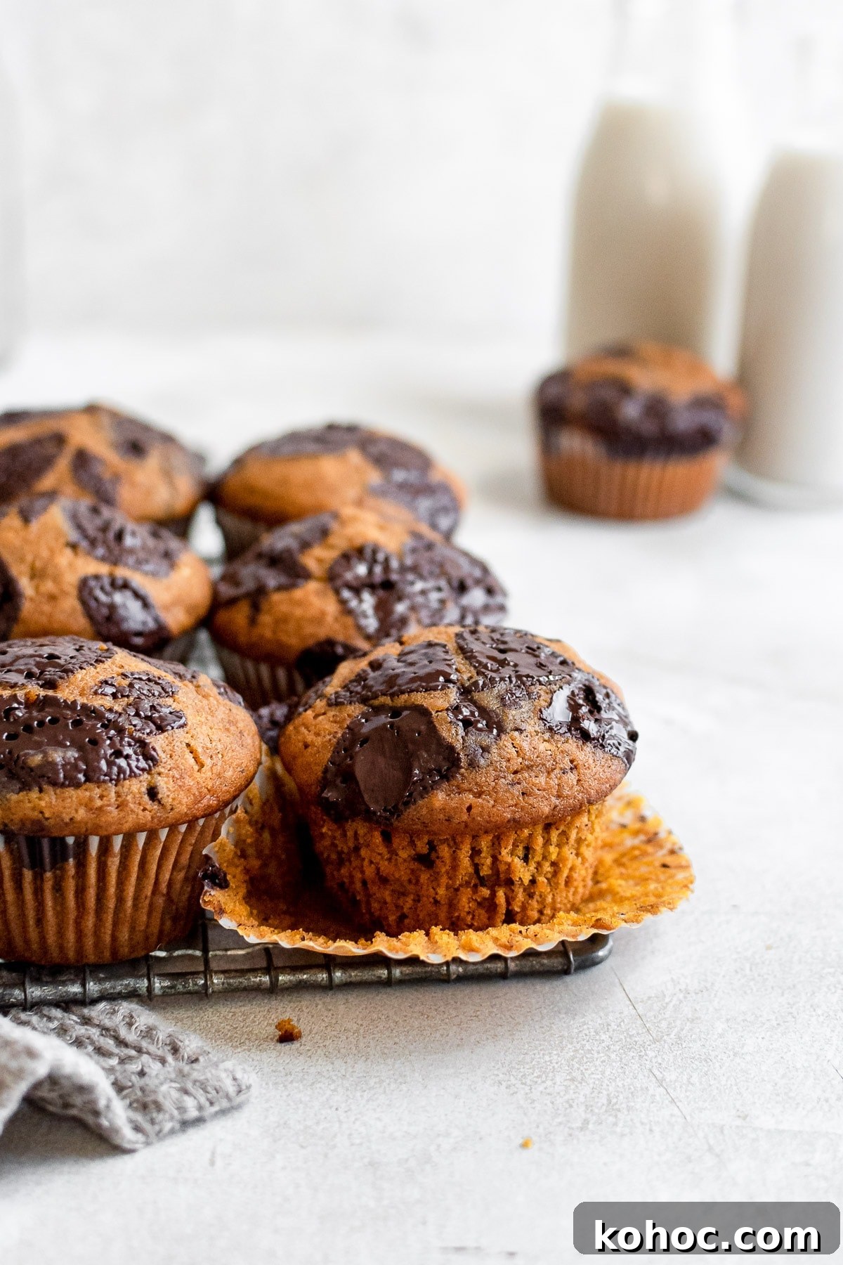 Moist Pumpkin Chocolate Chip Muffins 5 pumpkin muffins on wire rack with one muffin with missing wrapper