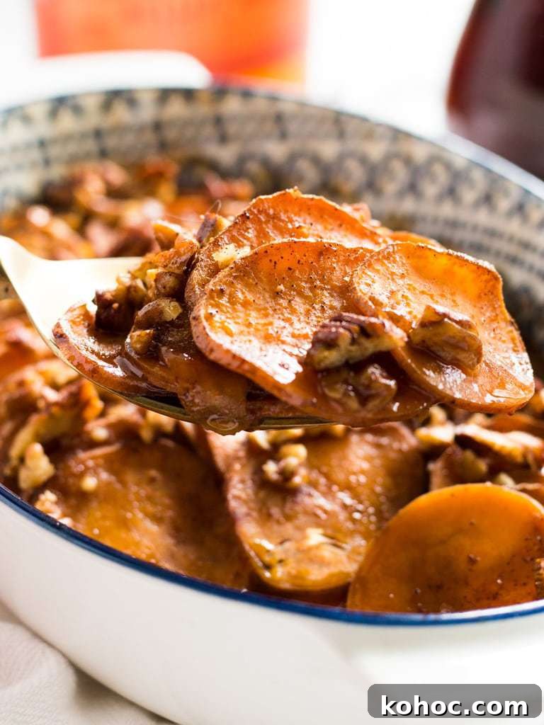 Bourbon Maple-Glazed Sweet Potatoes 4 serving spoon holding sweet potato rounds with pecans and glaze in a casserole dish.