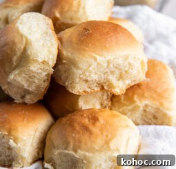 fluffy homemade dinner rolls in a pile on white cloth in basket