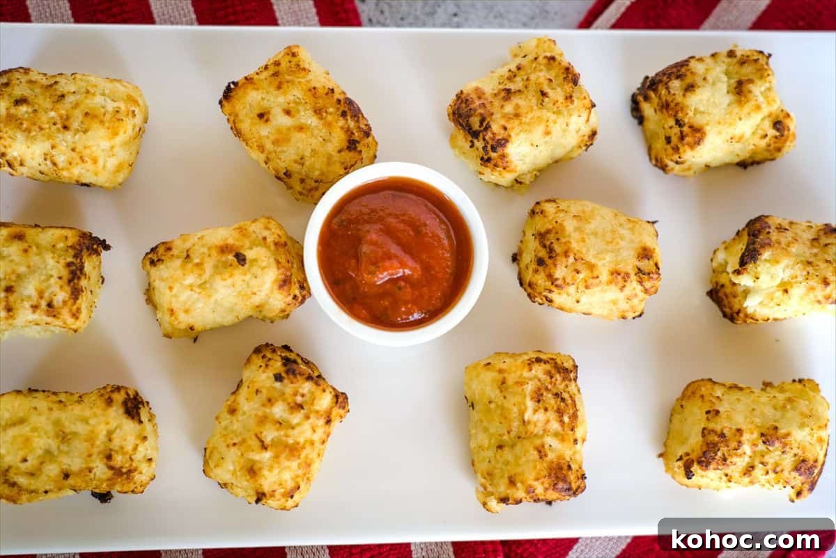 A rectangular plate of baked tater tots, including air fryer cauliflower tots, is arranged around a small cup of red dipping sauce.