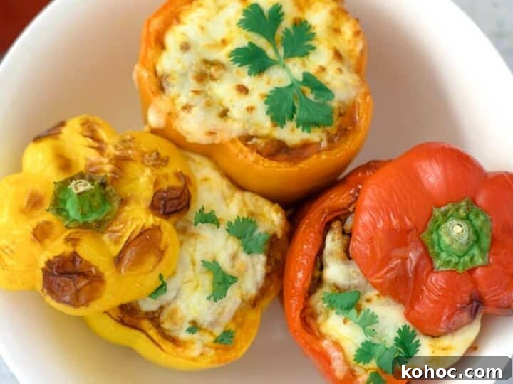 A white plate holds three air fryer stuffed peppers—two orange, one red—topped with melted cheese and garnished with cilantro.