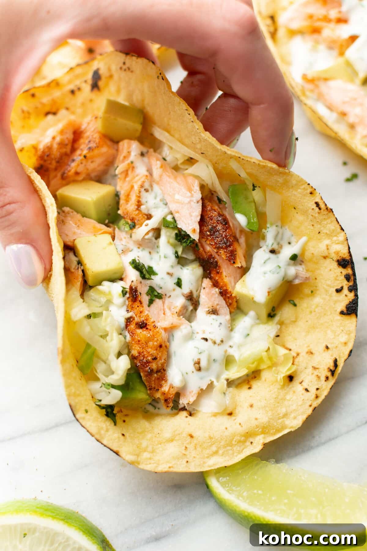 Crispy Baked Salmon Tacos with Lime Slaw 6 a female hand holding a baked salmon taco