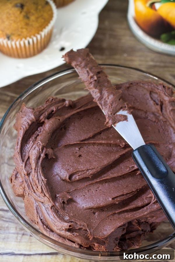 Moist Pumpkin Chocolate Chip Cupcakes with Cinnamon 5 Bowl of chocolate frosting with a plate of pumpkin chocolate chip cupcakes in the background.