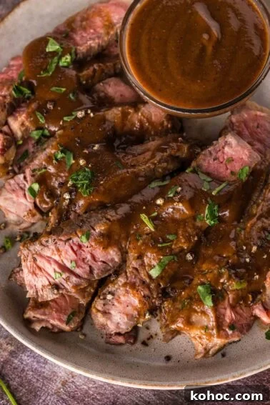 Sliced medium-rare steak topped with a1 sauce, garnished with chopped herbs, served on a plate with extra sauce in a small bowl.