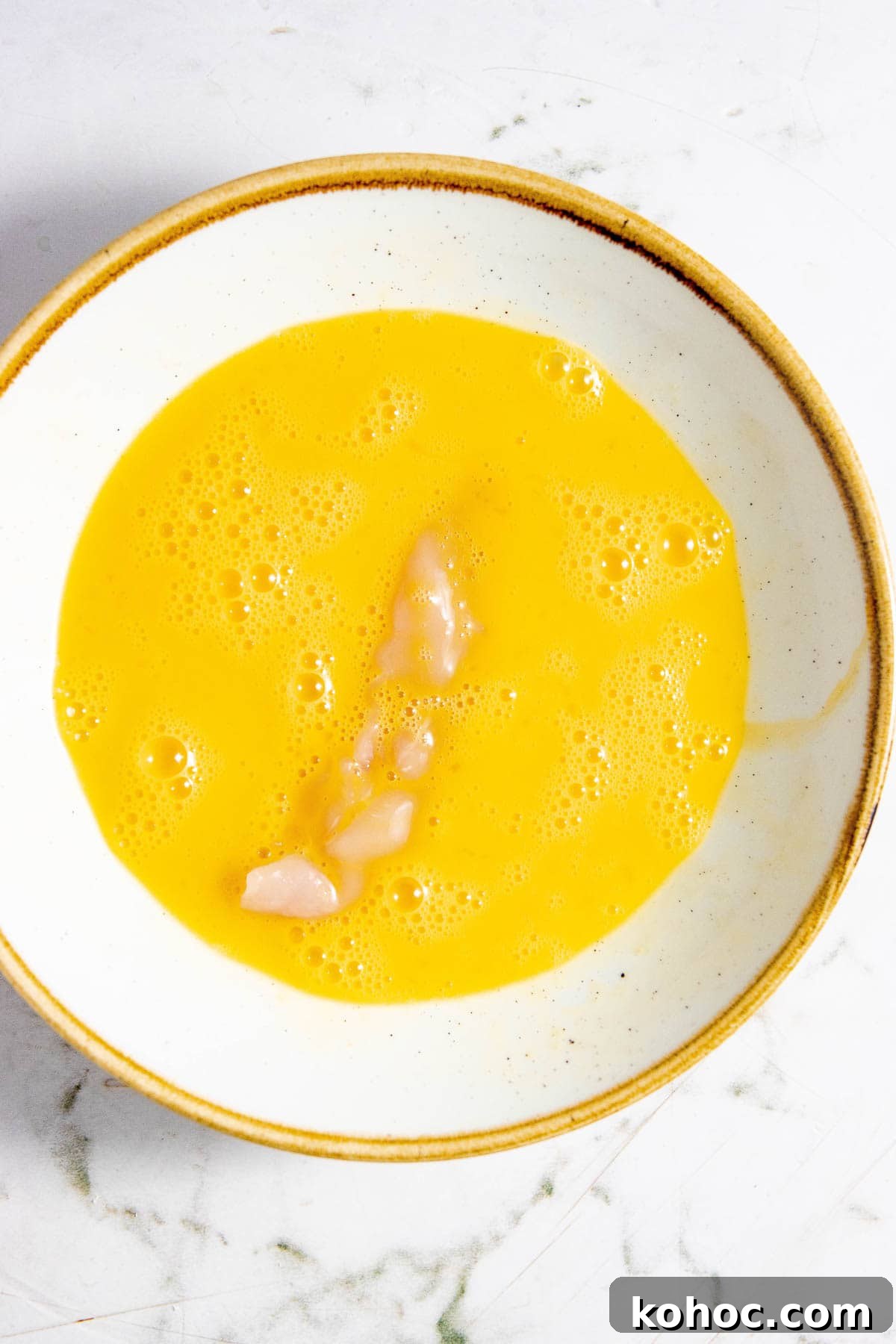 An bowl with chicken in an egg wash.