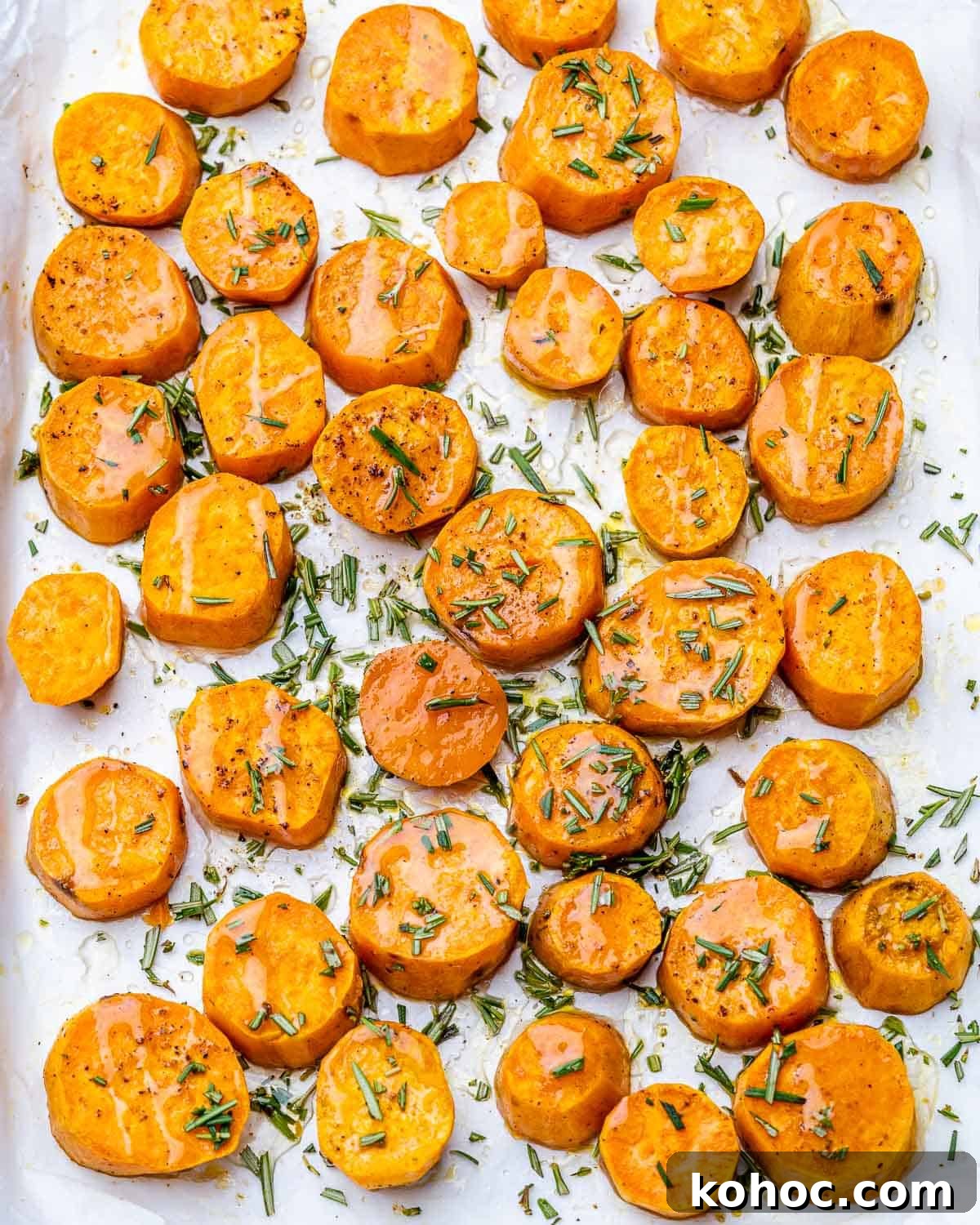 Crispy Roasted Sweet Potatoes with Garlic and Herbs 5 Sweet potato rounds drizzled with honey and garnished with rosemary on a pan.